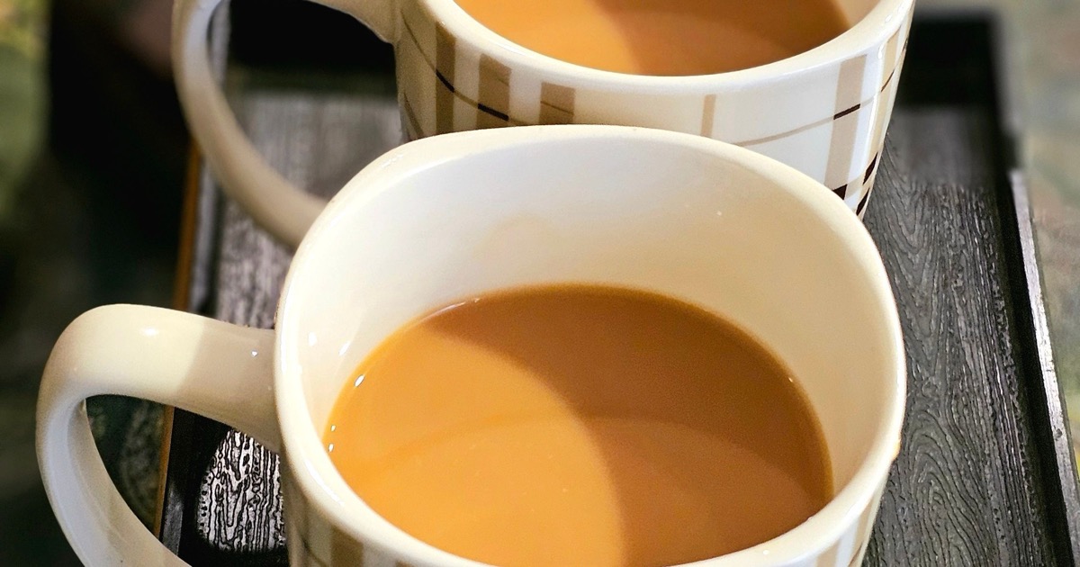 Two plaid-patterned mugs of milky tea on a dark wooden tray