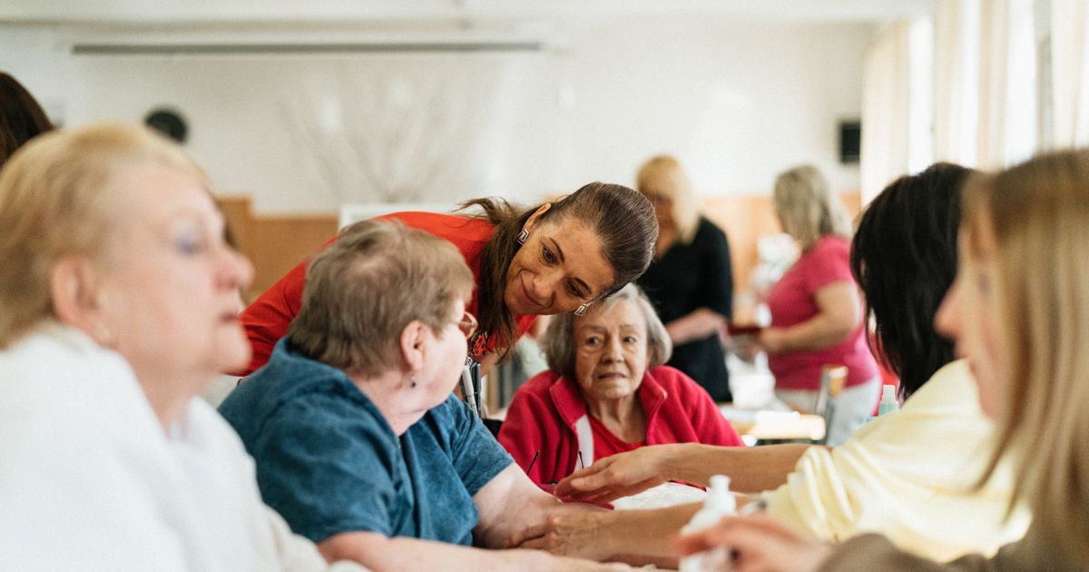 A caregiver leaning in to talk with a group of older people sitting around a table