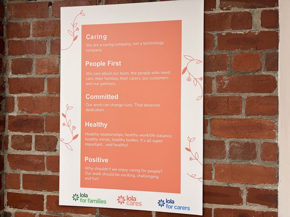 Our values poster on the office's brick wall: Caring, People First, Committed, Healthy and Positive, each with a line explaining what it means to us