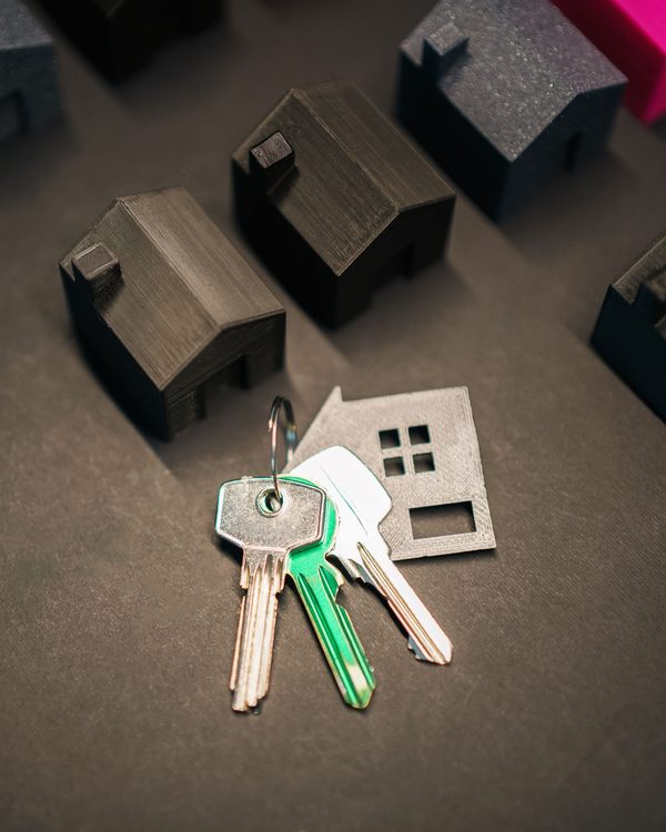A bunch of keys and a house-shaped key fob on a dark surface, surrounded by small model houses
