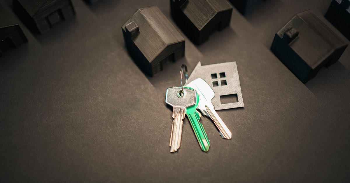 A bunch of keys and a house-shaped key fob on a dark surface, surrounded by small model houses